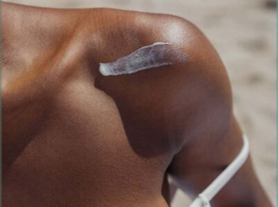 very sun tanned girl with a swab of sunscreen on her shoulder